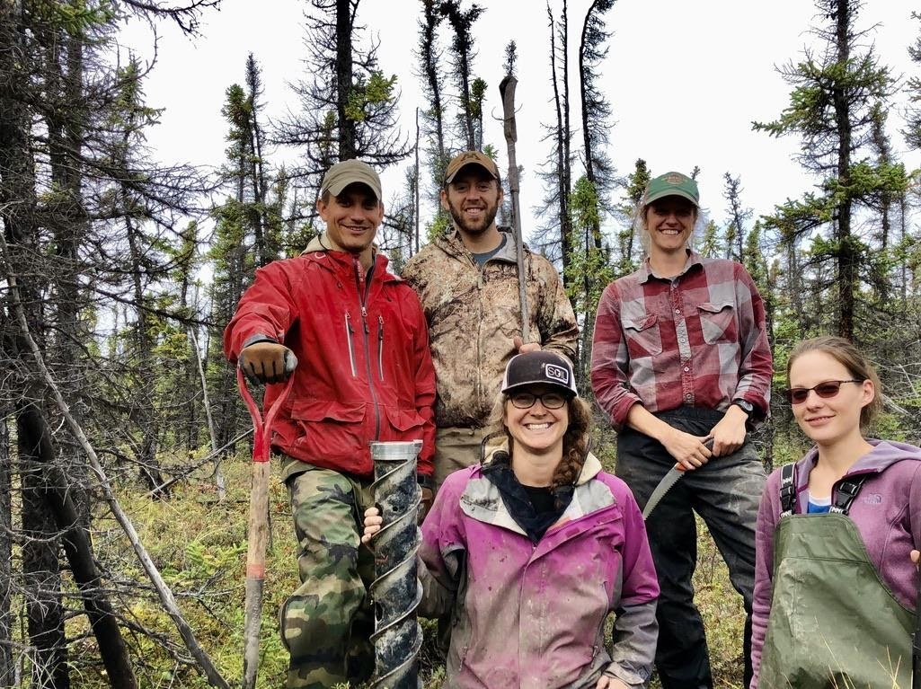 A photo of Prof. Nic Jelinski, Mike Sousa, and several lab mates standing in a forest with shovels 