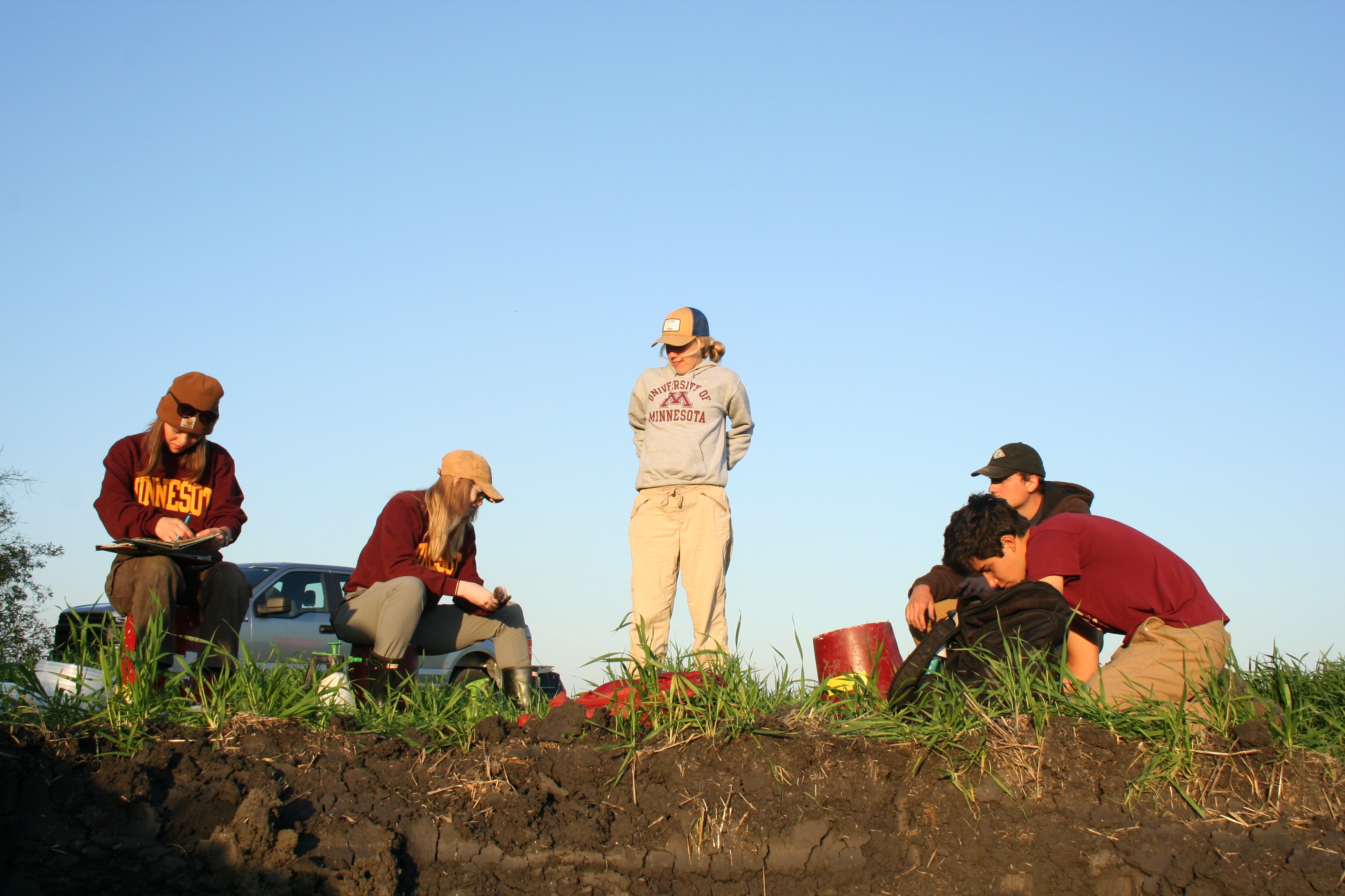 A photo of LAAS graduate student Megan Andersen standing near a soil pit with UMN soil judging students working around her.