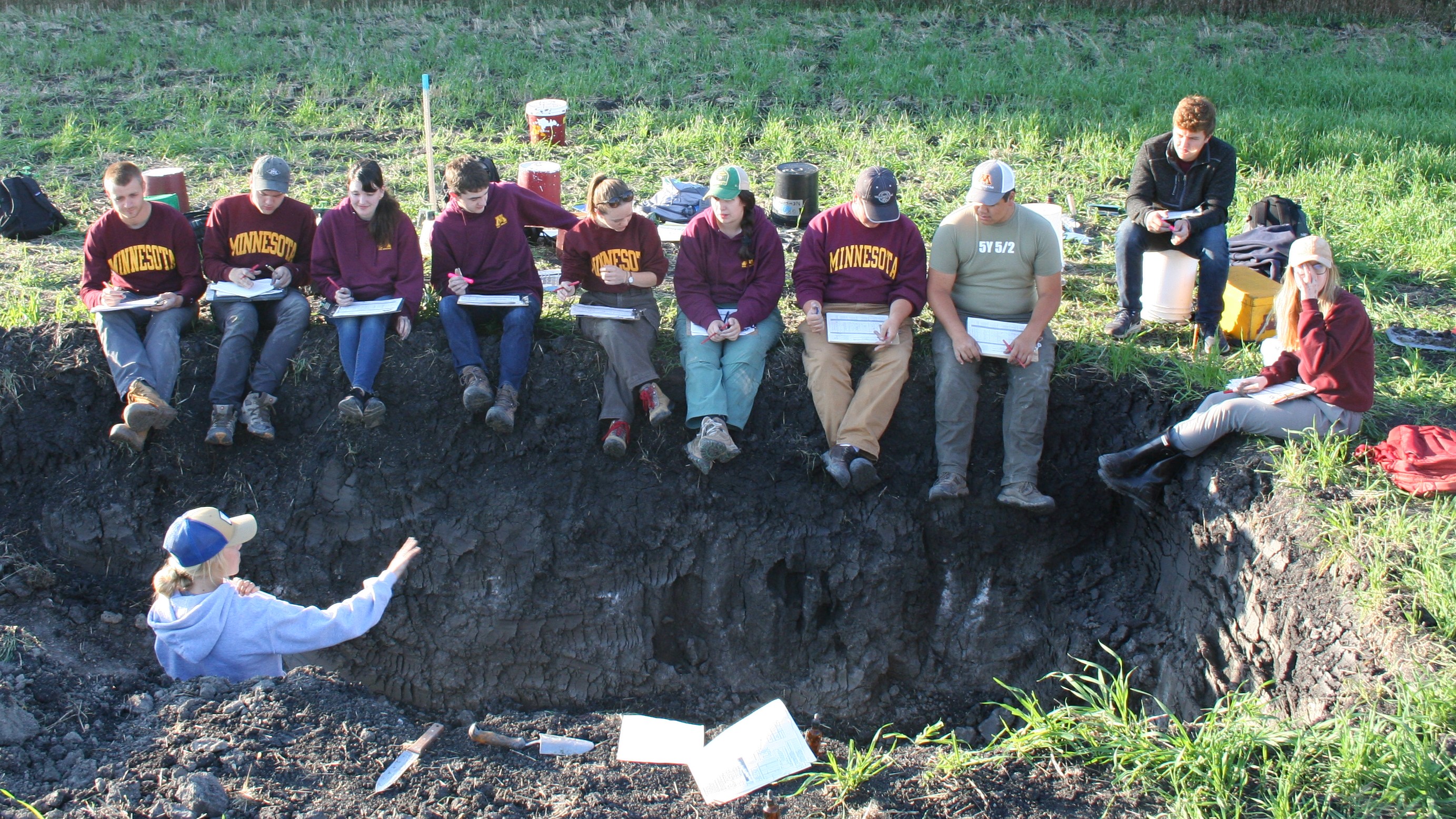 A photo of Megan Andersen, bottom left, in a soil pit surrounded by UMN soil judging students