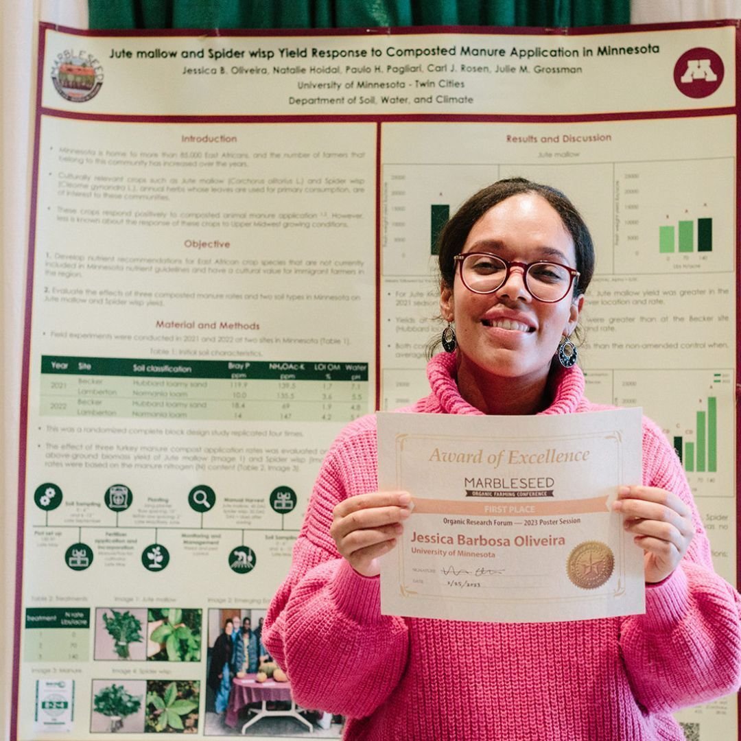 A photo of Jessica Barbosa Oliveira standing in front of her poster, holding an award